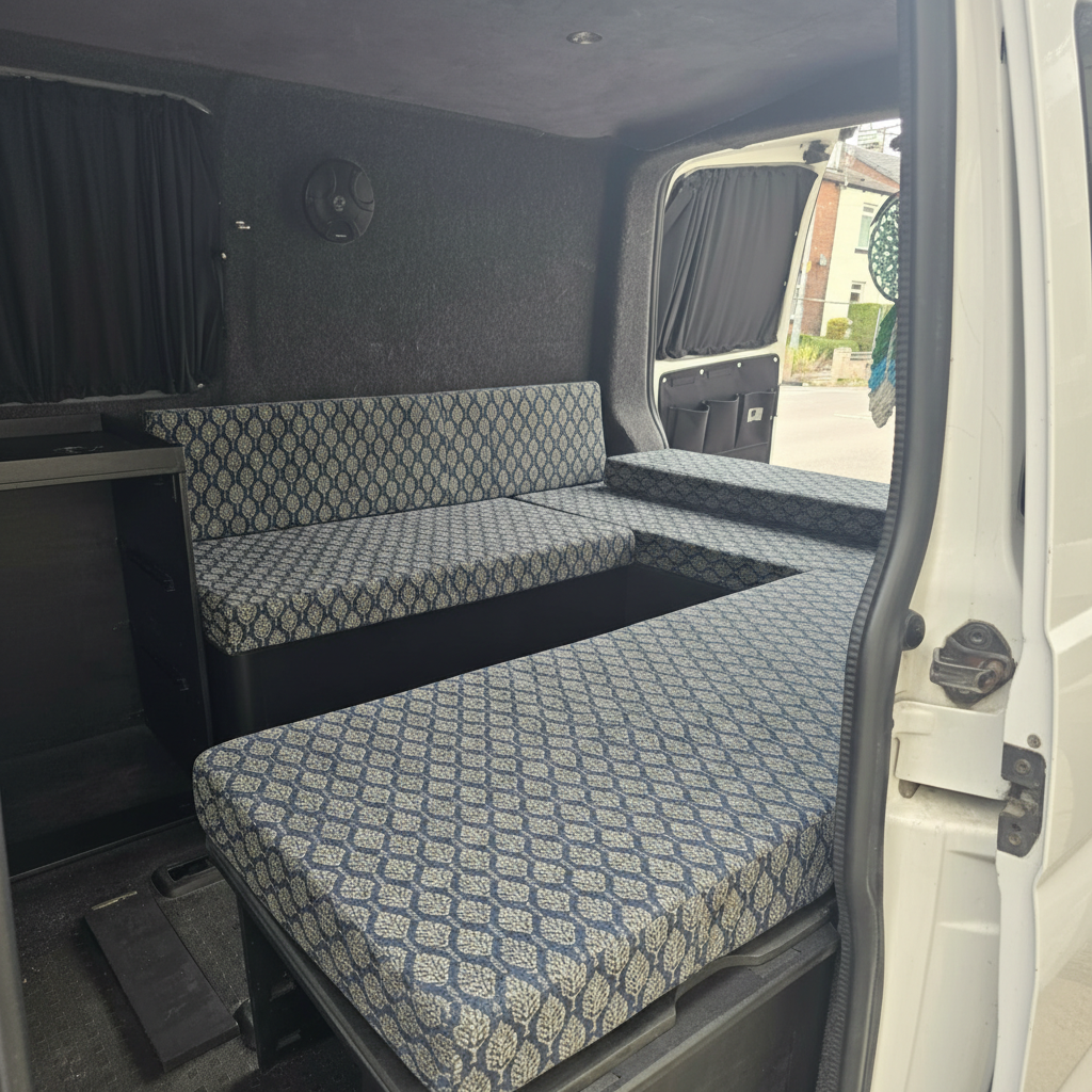 Contemporary slate blue geometric leaf Campervan cushions in stealth van-Modern Stealth Van Upholstery on U-shaped seating area-Blue and grey geometric pattern motorhome foam pads-High density foam cushions for VW Transporter conversion-Practical utility style camper interior with dark carpet lining